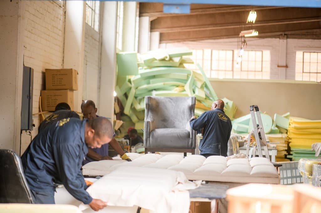 Several craftspeople at work on upholstered pieces in a bright workshop.