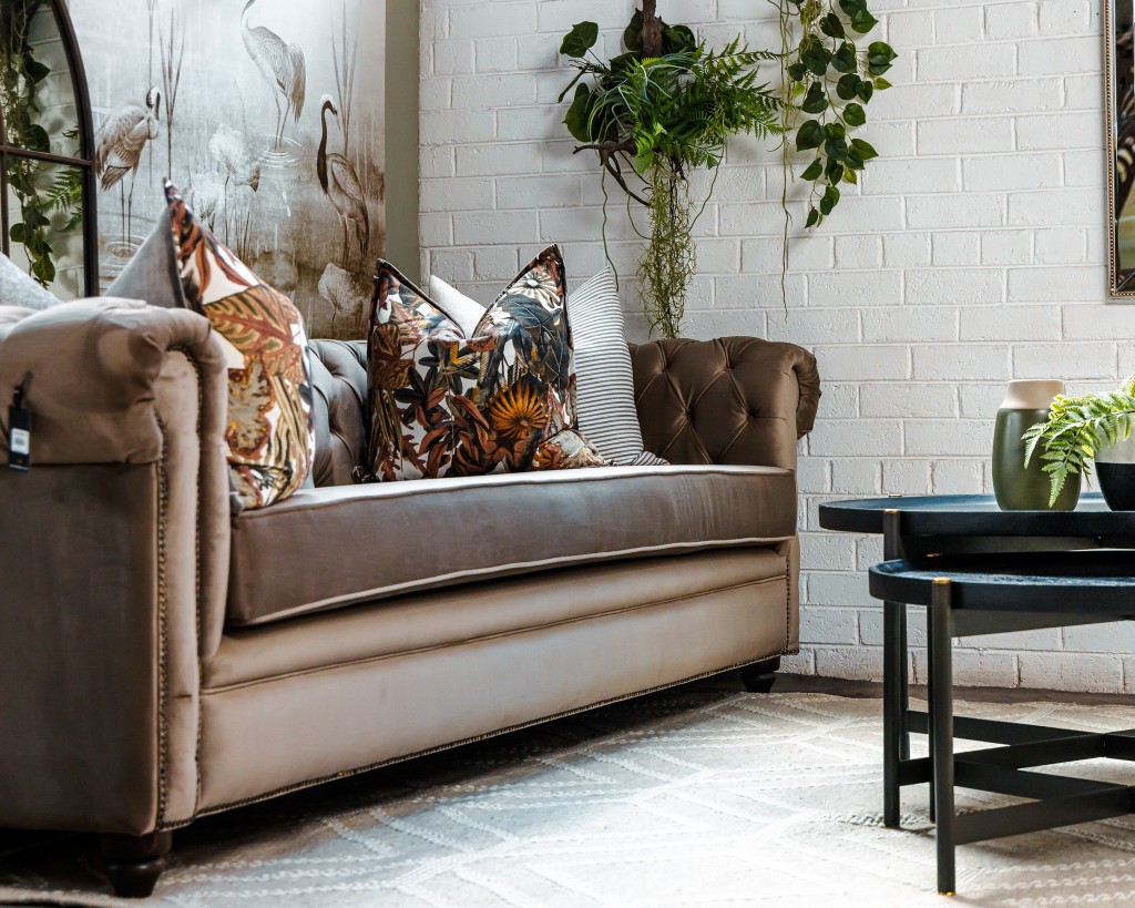Tufted sofa with botanical cushions against a white brick wall